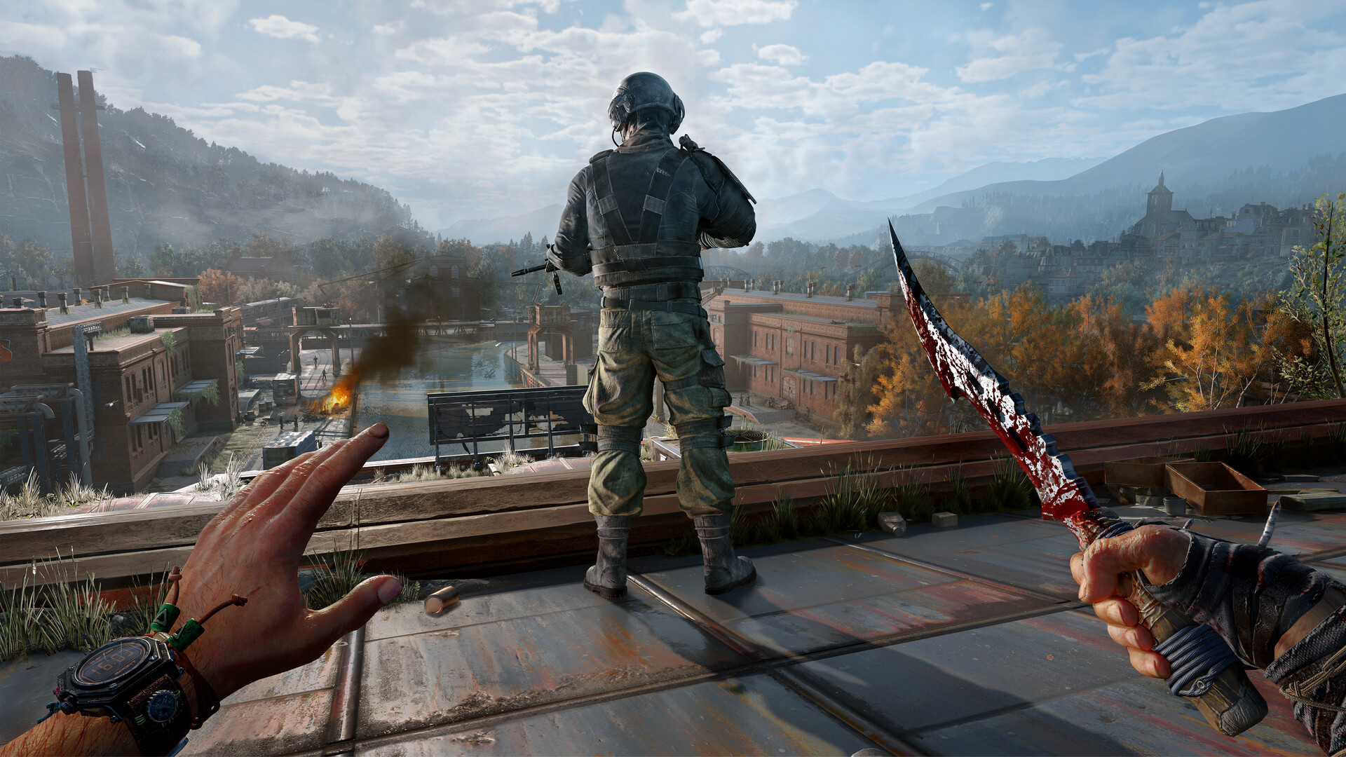 Dying Light: The Beast — First-person perspective of a character wielding a bloody knife on a rooftop, observing a second character in tactical gear. The scene overlooks an industrial zone with distant hills and buildings under a cloudy sky.