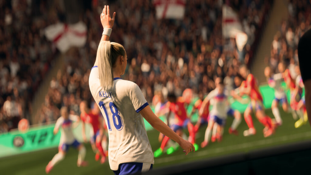 Female soccer player Kelly #18 raising her hand during a match, with teammates and spectators in the background.